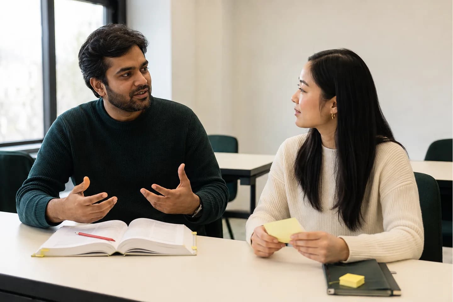Two learners have a conversation while an open language reference book remains available beside them